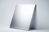 Stack of brushed aluminum sheets leaning against a light gray wall on a smooth surface.