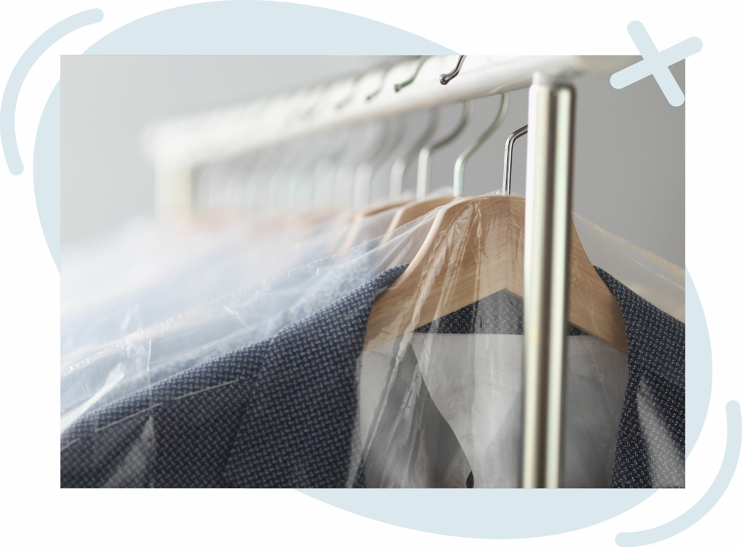 Close-up of suits on wooden hangers covered with clear plastic garment bags on a metal clothing rack.