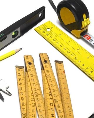 Assorted measuring tools on a white surface, including tape measures, rulers, a spirit level, caliper, and pencils.