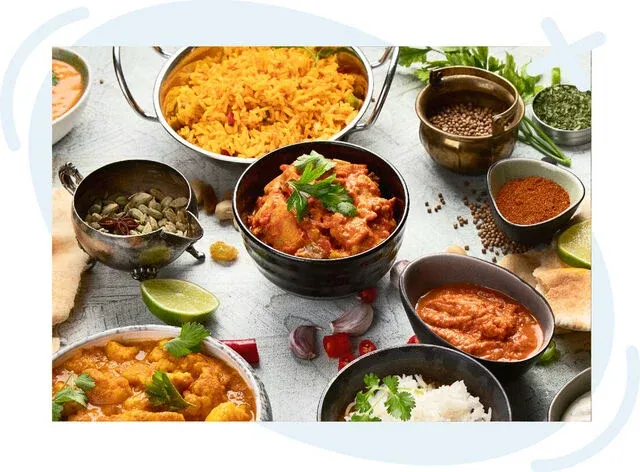 Assorted Indian dishes and spices arranged on a table, including curries, yellow rice, chutneys, and whole spices.