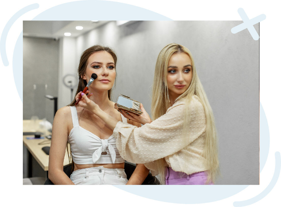 Makeup artist applying blush to a seated woman in a modern studio.