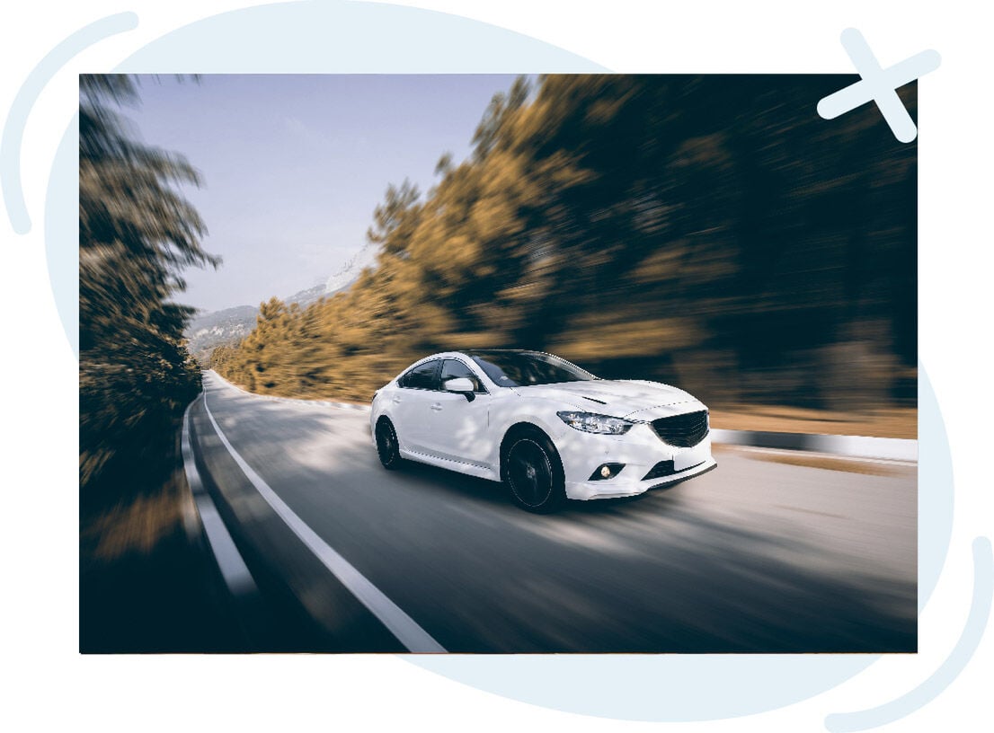 White sedan driving quickly on a curving mountain road with motion blur in the trees and pavement.