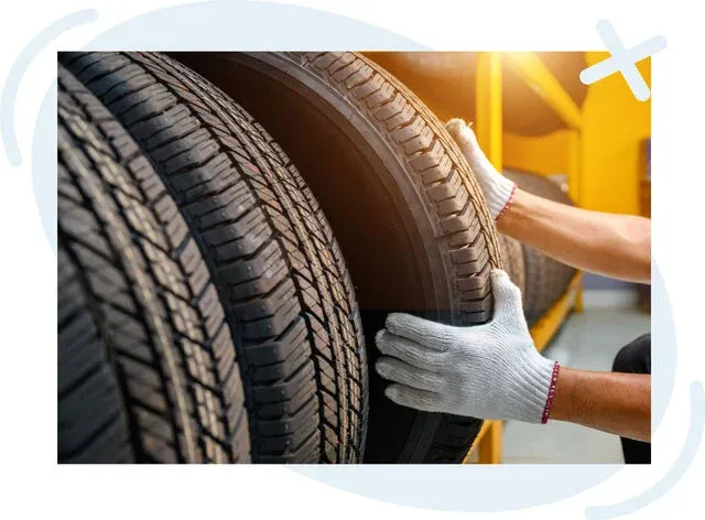 Gloved hands arranging a stack of car tires on a rack in a brightly lit workshop.