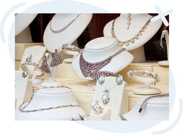 Display of elegant jewelry sets on white stands in a boutique window, including necklaces, earrings, bracelets, and rings with sparkling stones.