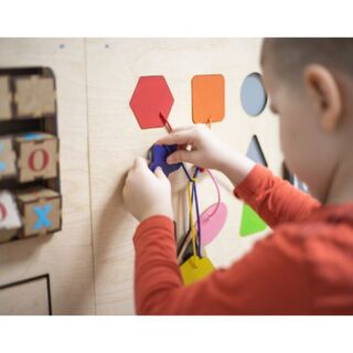 Child playing with a wooden activity board, threading colorful shapes with laces.