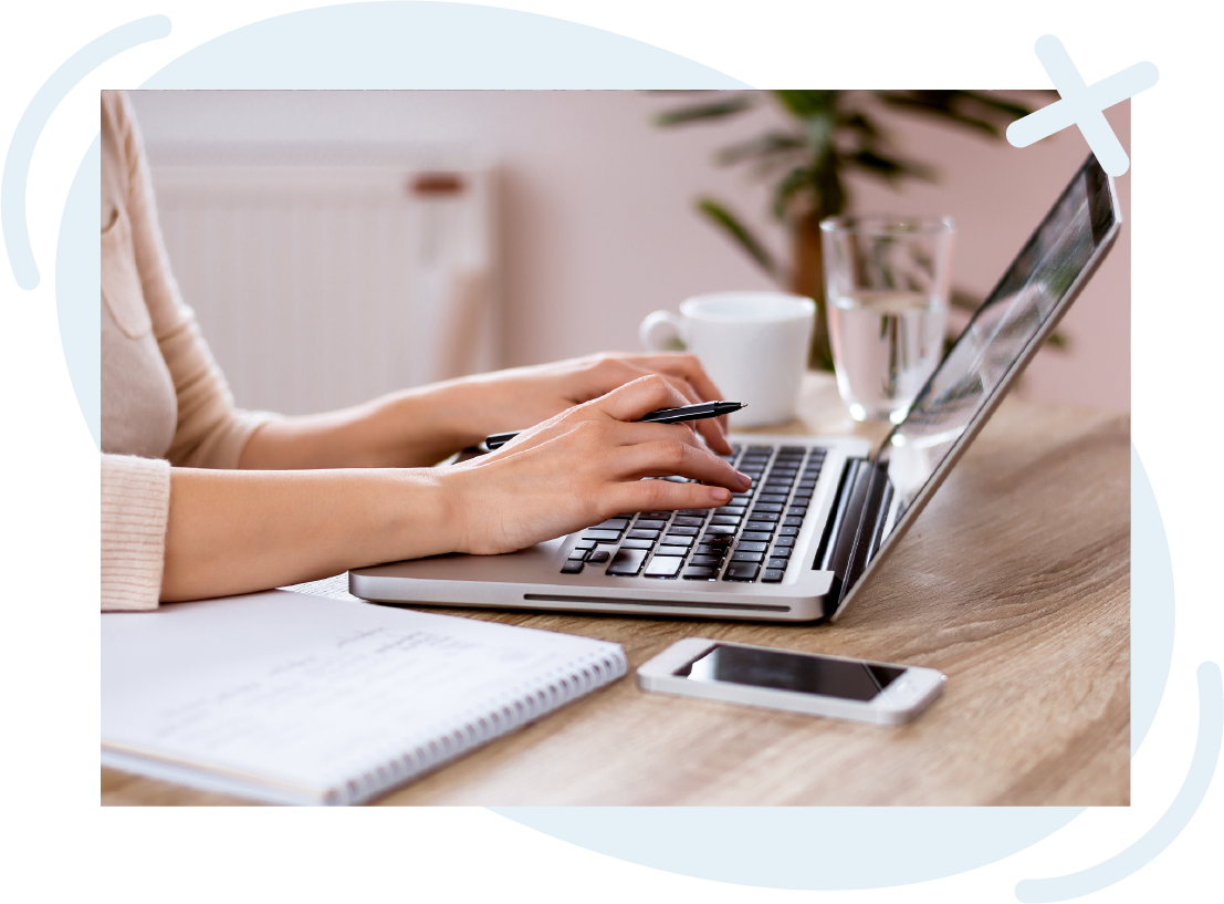 Hands typing on a laptop at a tidy desk with notebook, smartphone, and coffee cup.