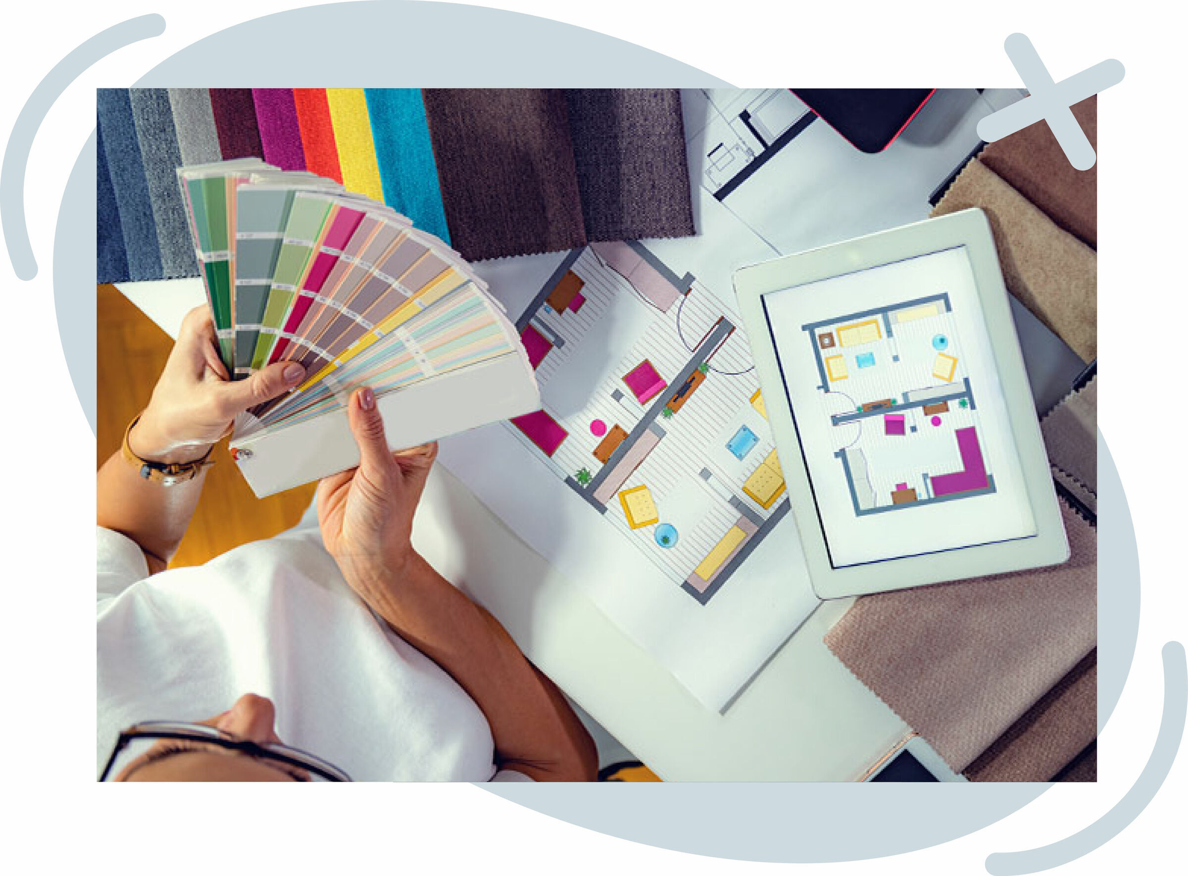 Person selecting paint colors from a swatch fan while reviewing interior design floor plans on paper and a tablet.