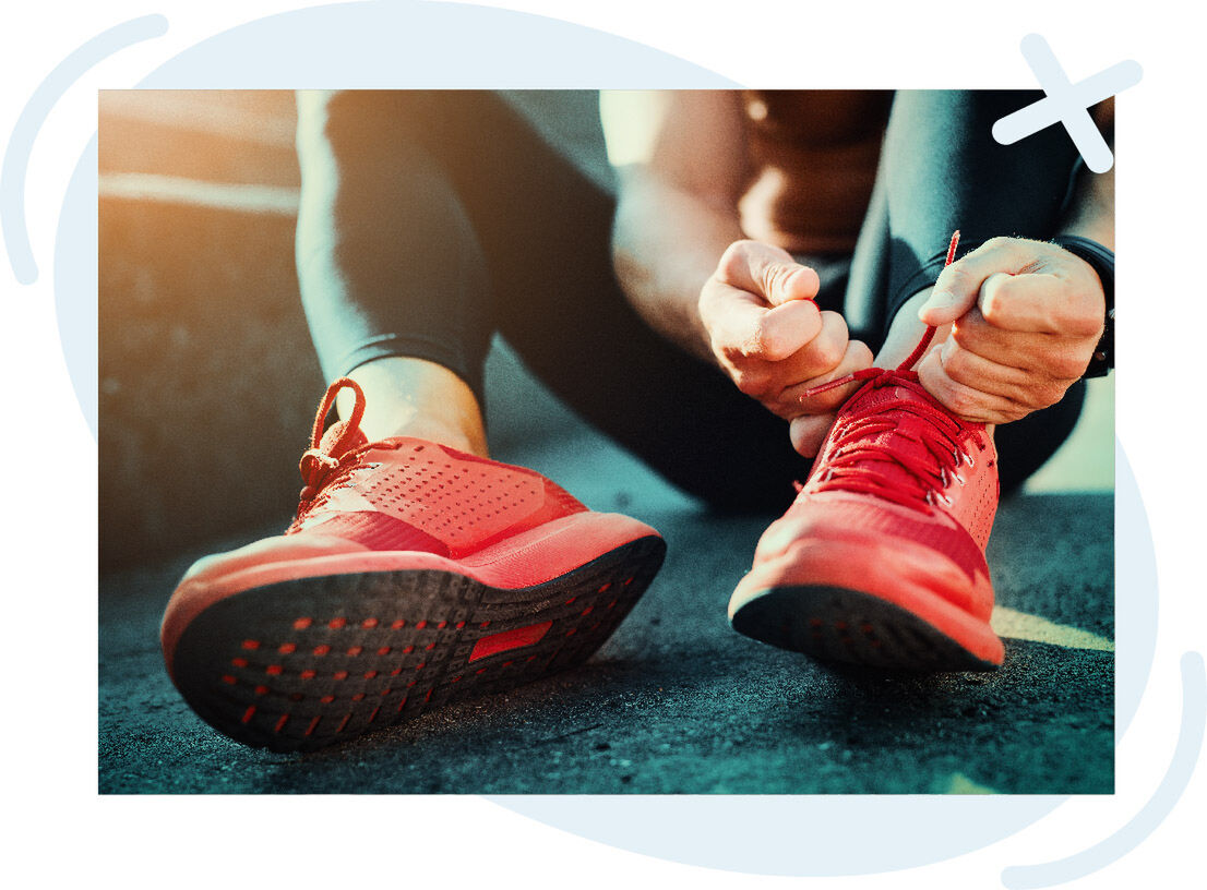 Close-up of a person tying the laces on bright red running shoes while sitting on the ground outdoors.