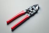 Close-up of a pair of bolt cutters with red handles on a light gray surface.
