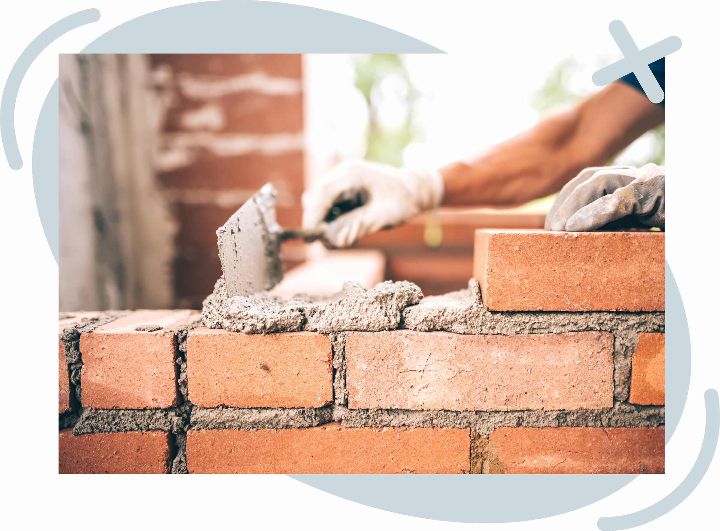 Close-up of a bricklayer building a wall, spreading mortar with a trowel and placing red bricks, with gloved hands in focus and a soft, bright background.