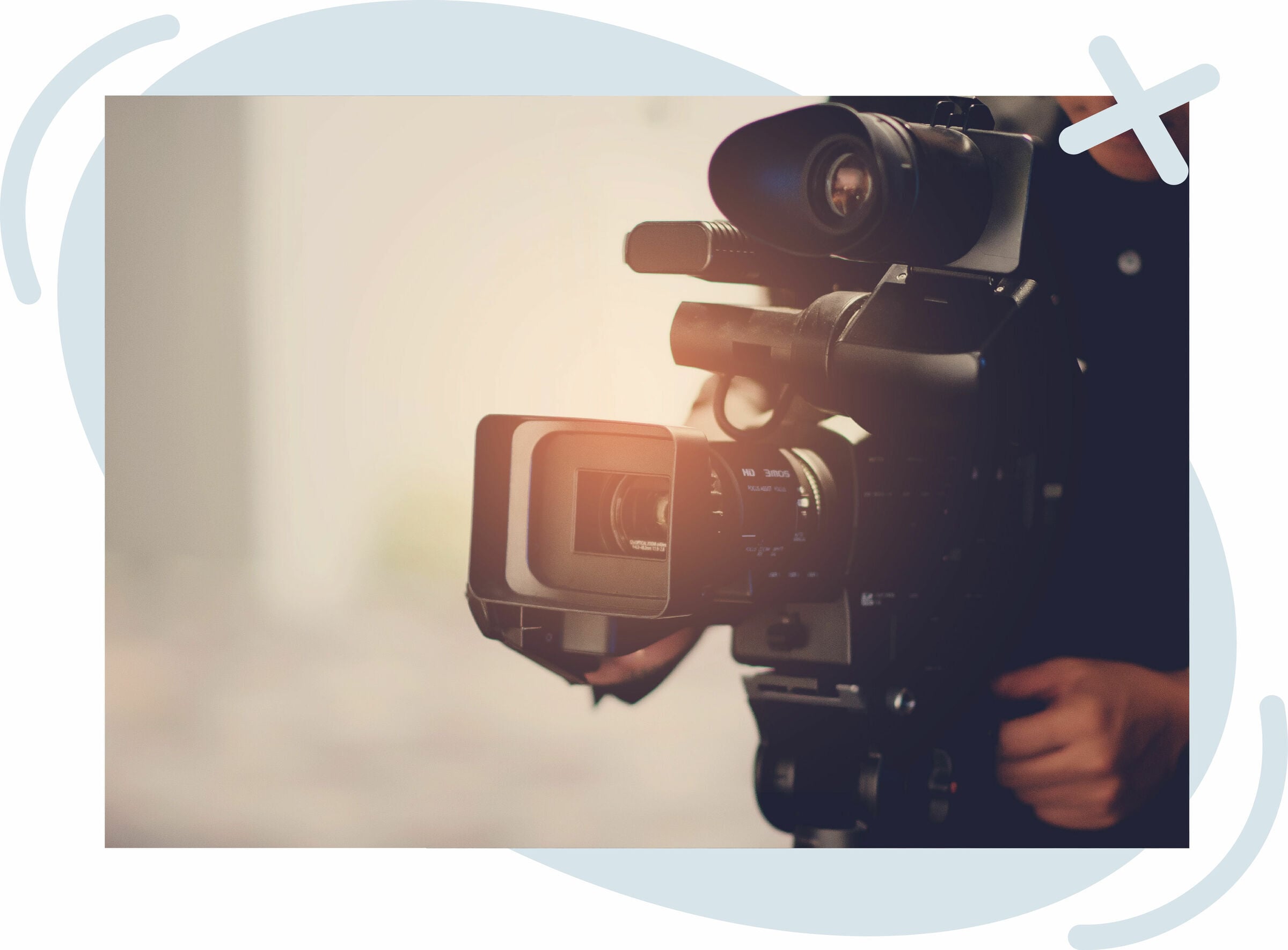 Close-up of a professional video camera being operated indoors with warm light flare.