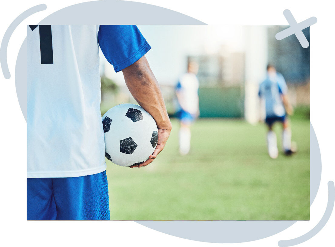 Soccer player holding a ball at their side on a field, with teammates in the background out of focus.