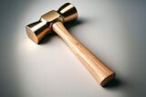 Polished brass double-faced mallet with a smooth wooden handle on a neutral background