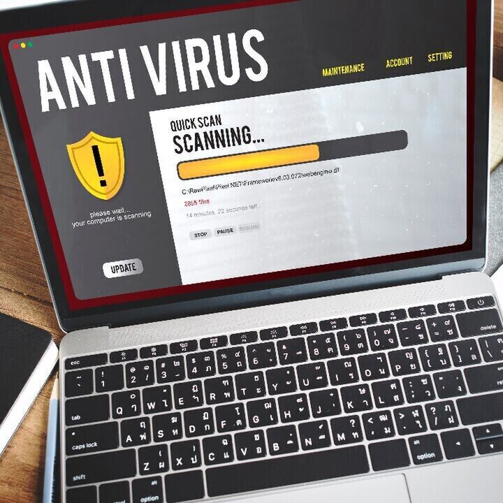 Laptop on a wooden desk displaying an antivirus program running a quick scan with a progress bar.