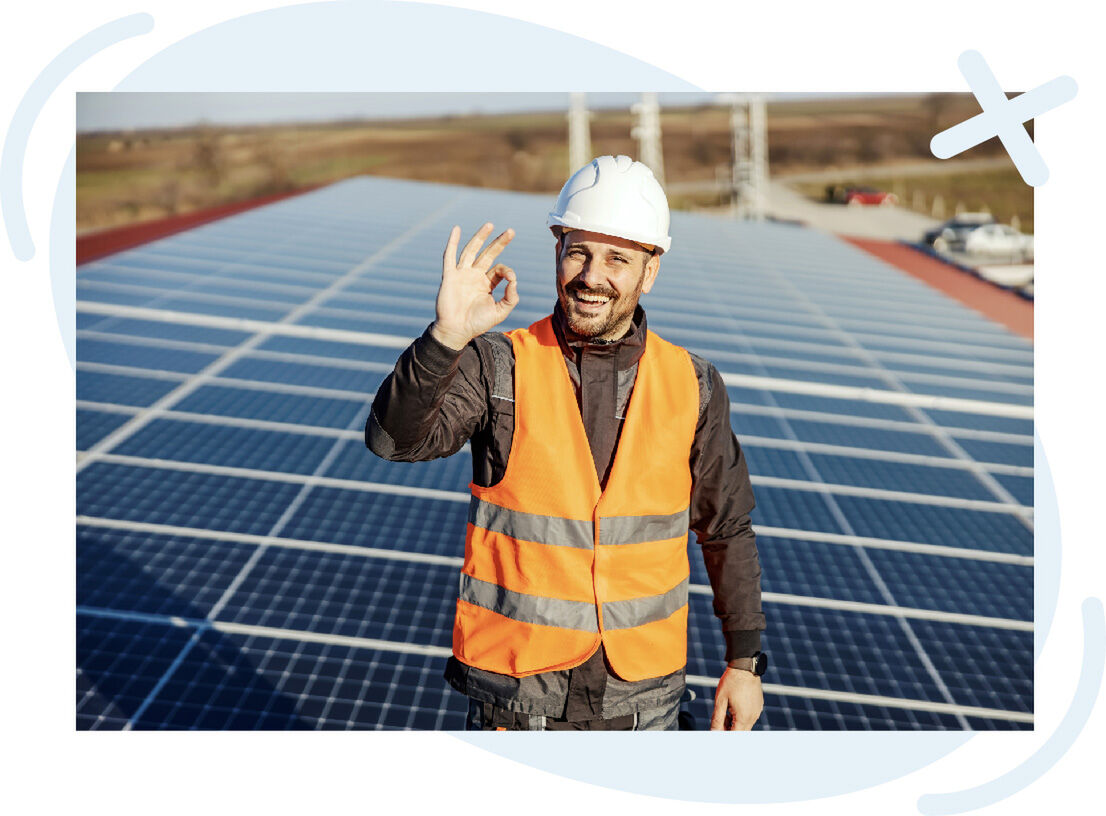 Smiling solar technician on a rooftop array giving an OK hand gesture.
