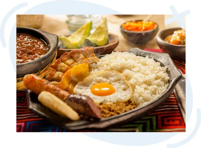 Hearty Colombian meal with rice, fried egg, beans, plantain, chorizo, pork cracklings, avocado, and sauces served on a rustic platter.