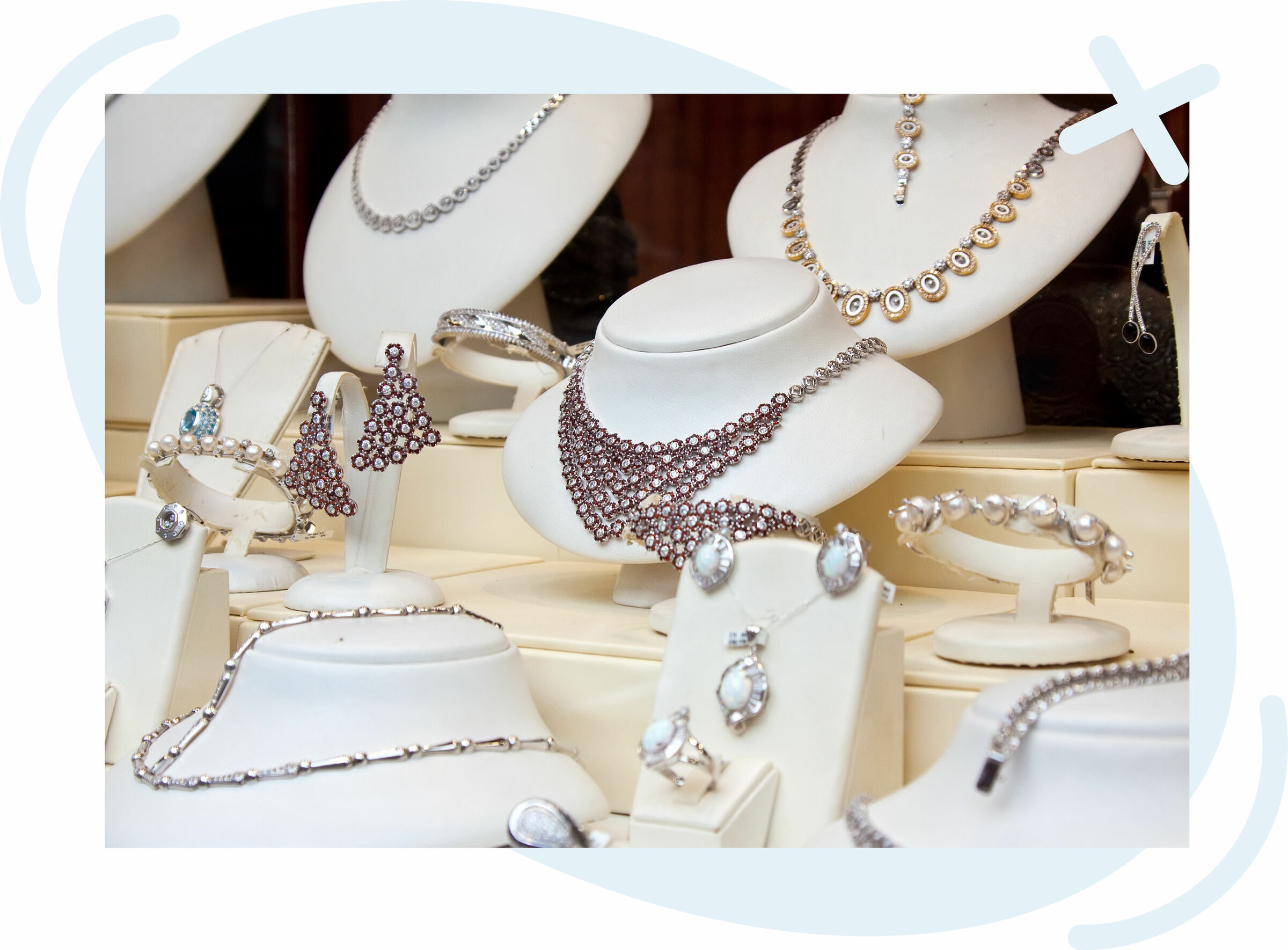 Display of elegant jewelry on white stands in a shop window, featuring layered necklaces, chandelier earrings, bracelets, and rings in silver and gold tones.
