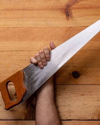 Hand holding a traditional hand saw against a wooden plank background.