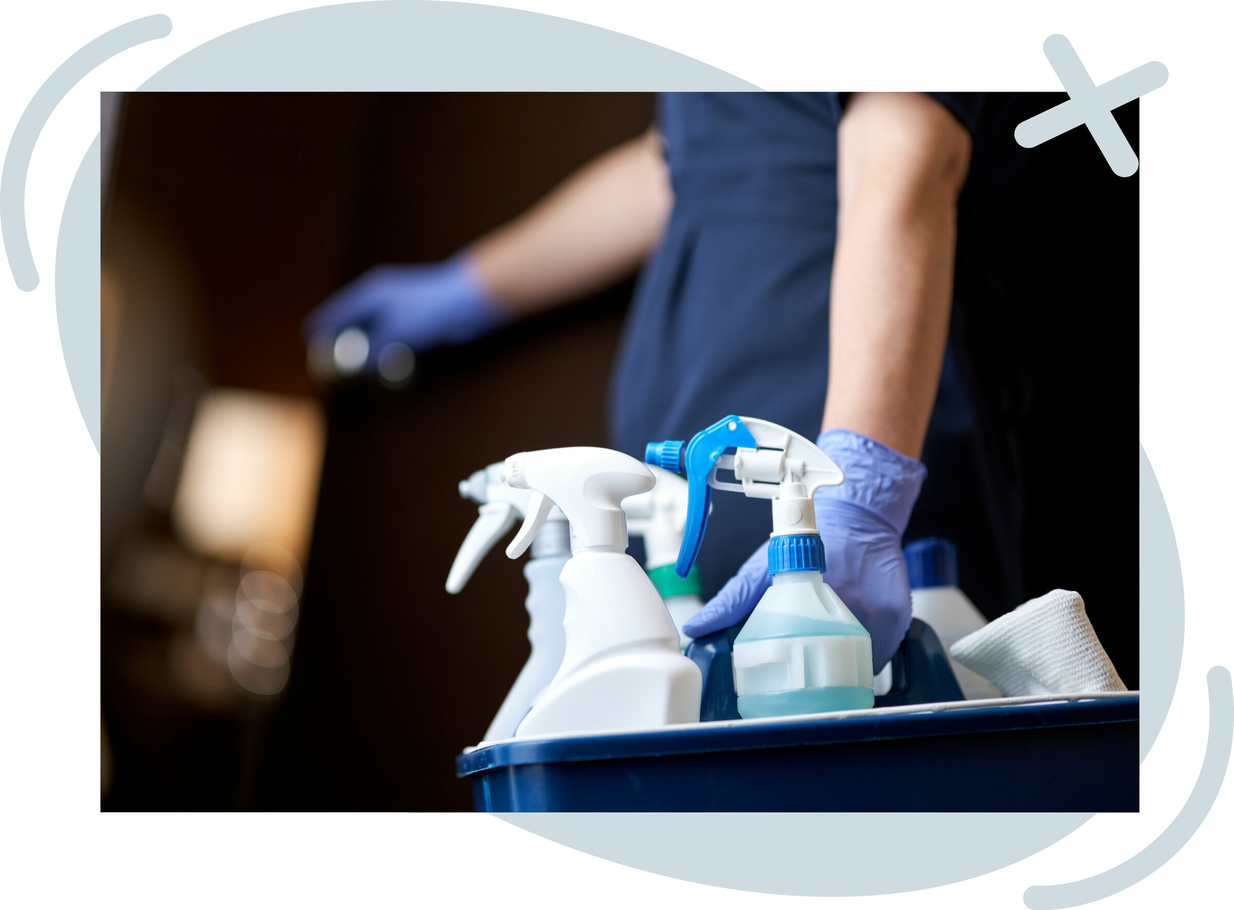 Close-up of a cleaning cart with spray bottles and supplies, handled by a person wearing purple gloves.