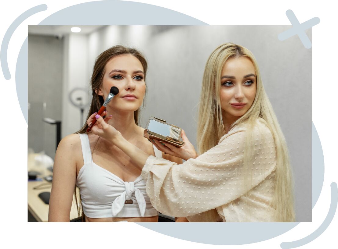 Makeup artist applying blush to a woman's cheek in a modern studio.