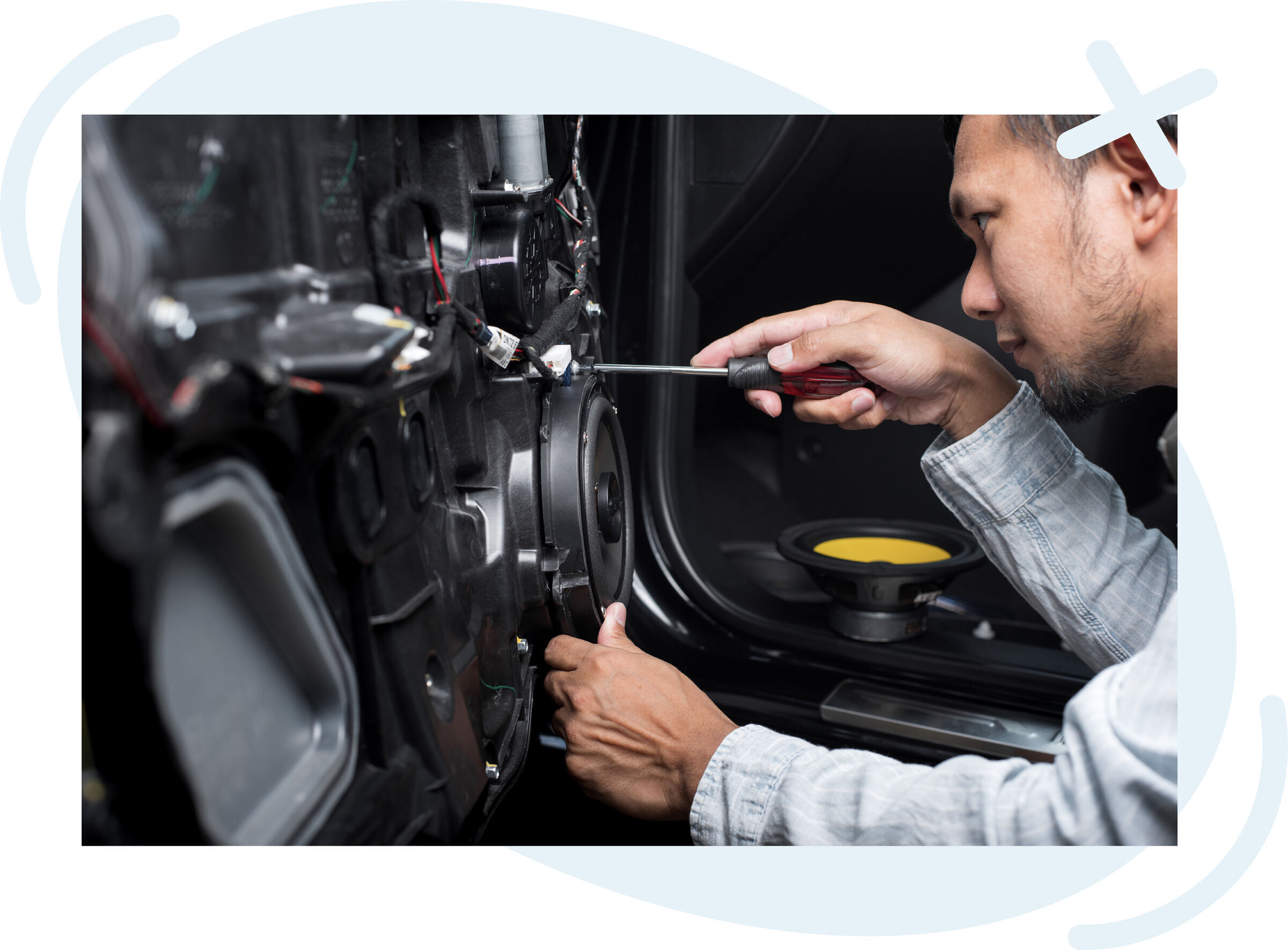 Technician installing a car door speaker using a screwdriver.