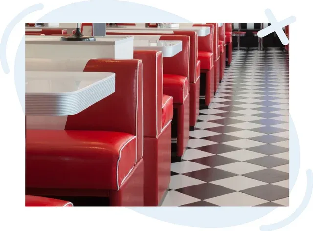 Row of glossy red diner booths with white tables beside a black-and-white checkered floor in a retro restaurant interior.