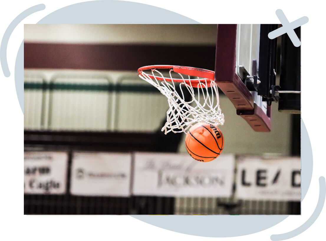 Close-up of an orange basketball dropping through a hoop and white net in an indoor gym.