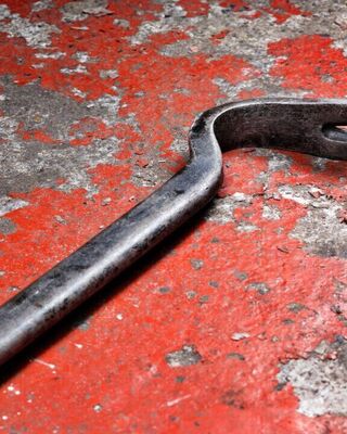 Close-up of a metal pry bar lying on a weathered red concrete surface with peeling paint and gray patches.