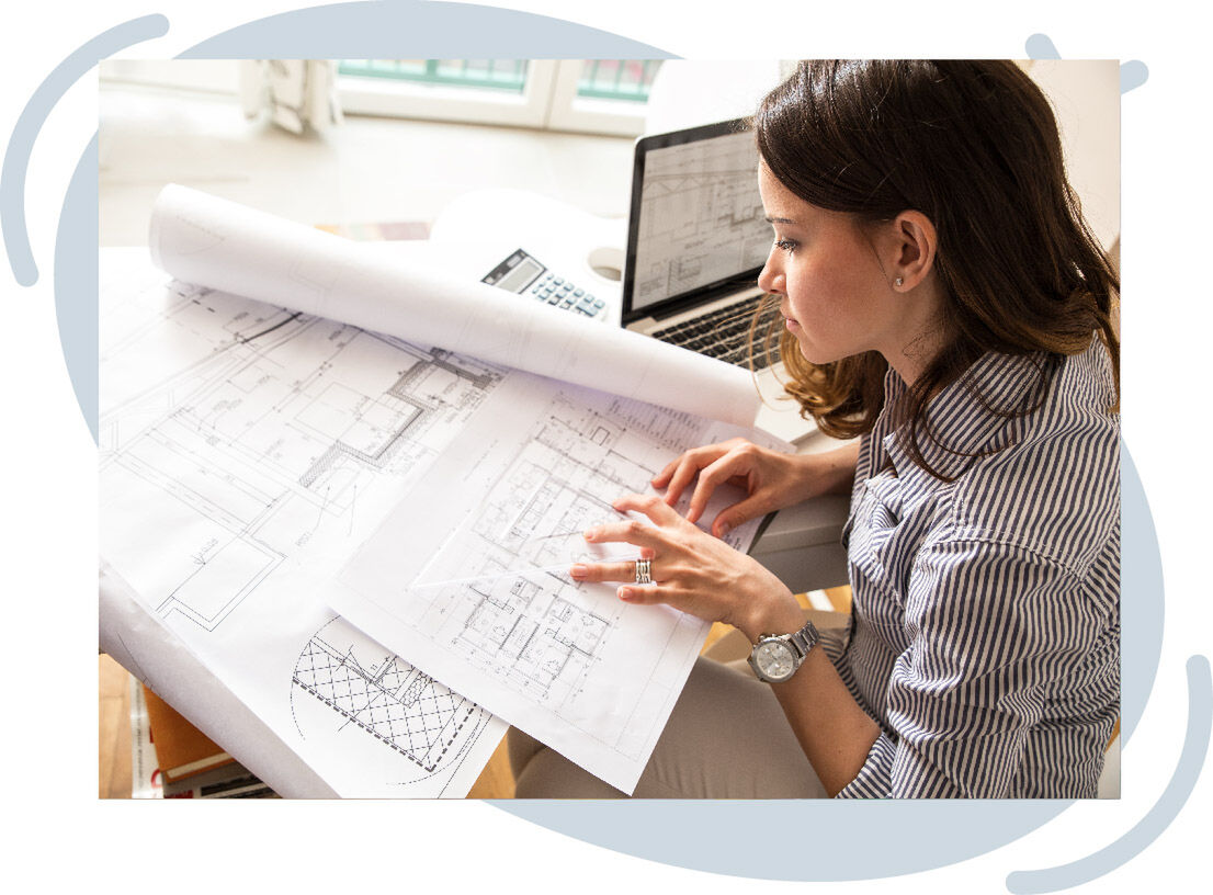 Person reviewing architectural blueprints at a desk with a laptop and calculator nearby.