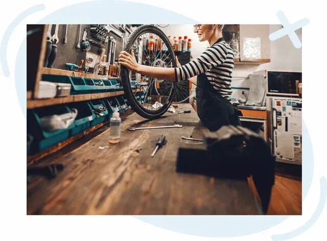 Mechanic in a bicycle repair workshop adjusting a detached bike wheel on a wooden workbench with tools and parts around.