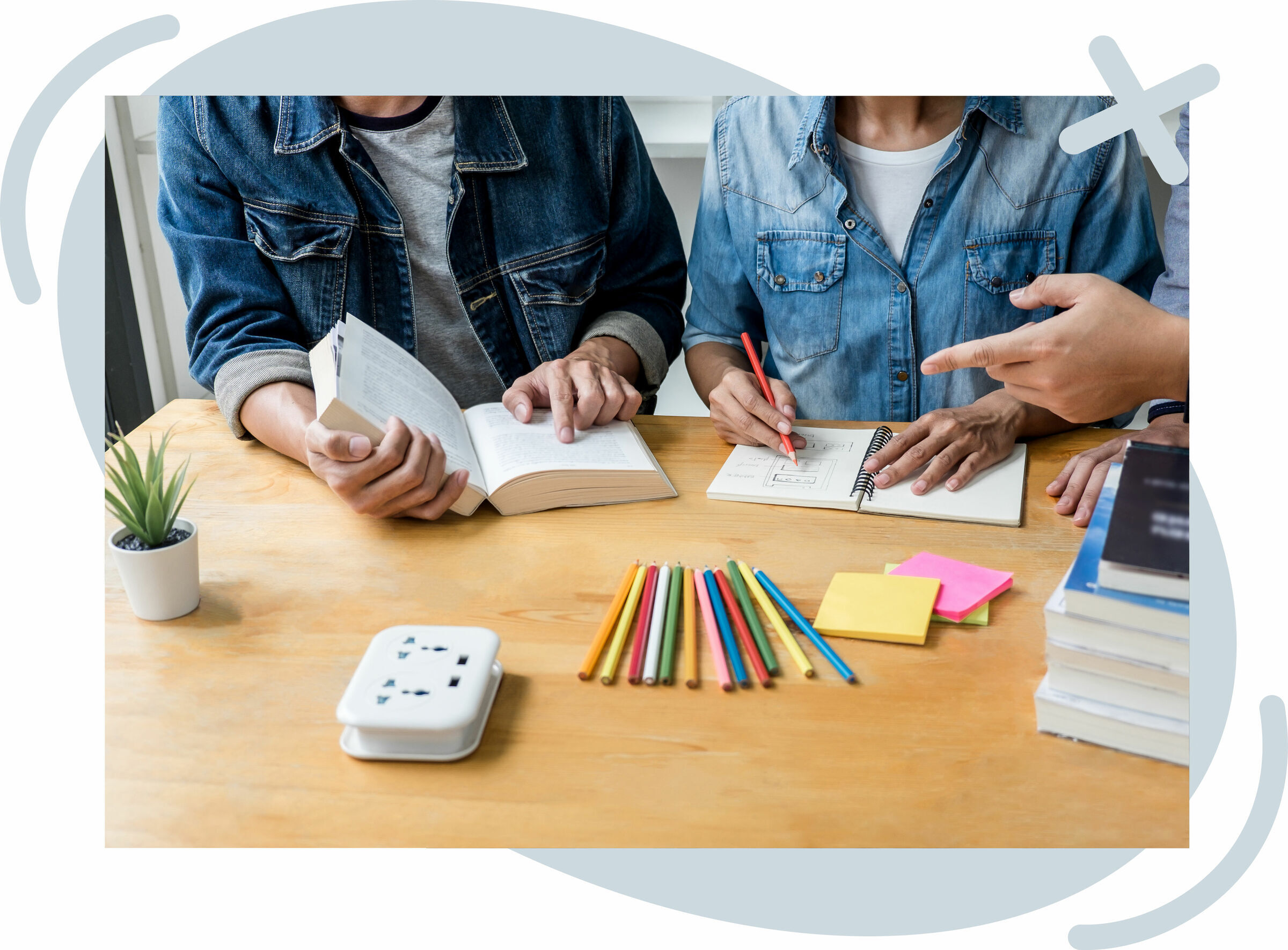 Students collaborating at a wooden table with books, notebooks, and colorful pencils