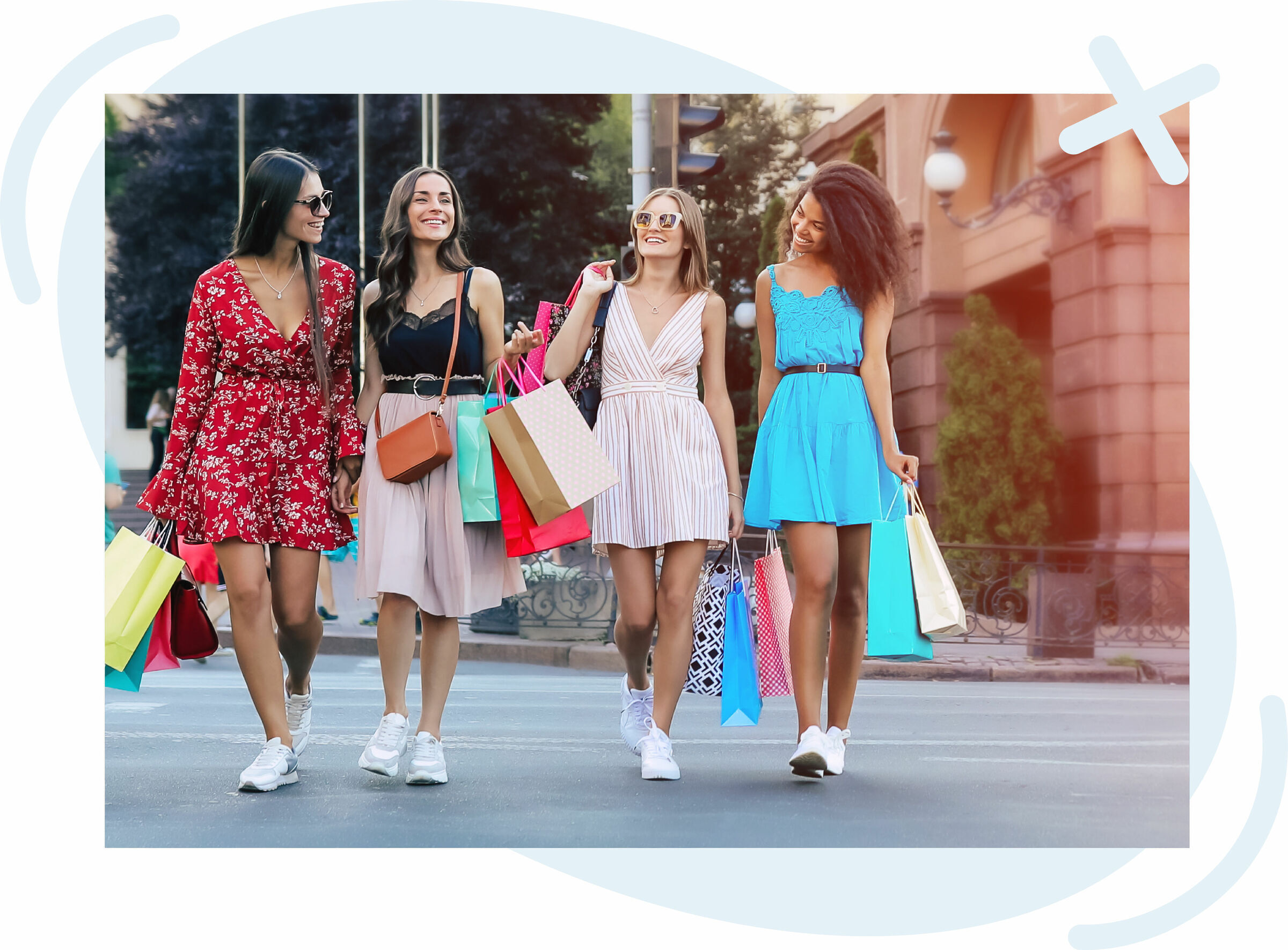 Four young women walking together outdoors after shopping, smiling and carrying colorful shopping bags while wearing stylish summer dresses and sneakers.