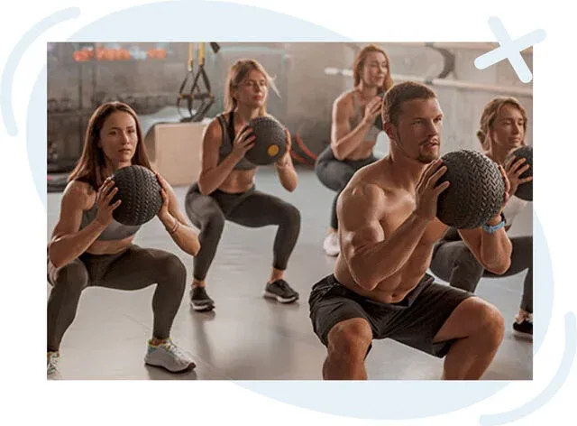 Group fitness class doing medicine ball squats in a gym.