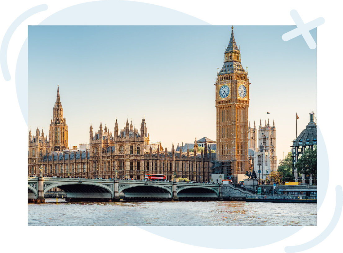 Riverside view of a historic clock tower and ornate parliamentary buildings beside a bridge at sunset.
