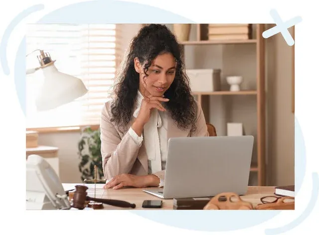 Professional woman at a desk working on a laptop in a well-lit office with notary tools nearby.
