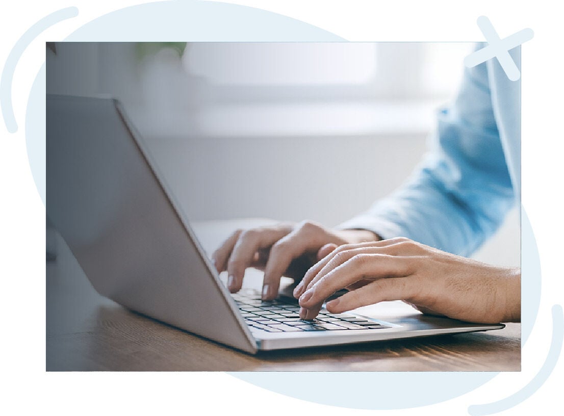 Close-up of a person typing on a laptop at a desk in a bright, softly lit room.