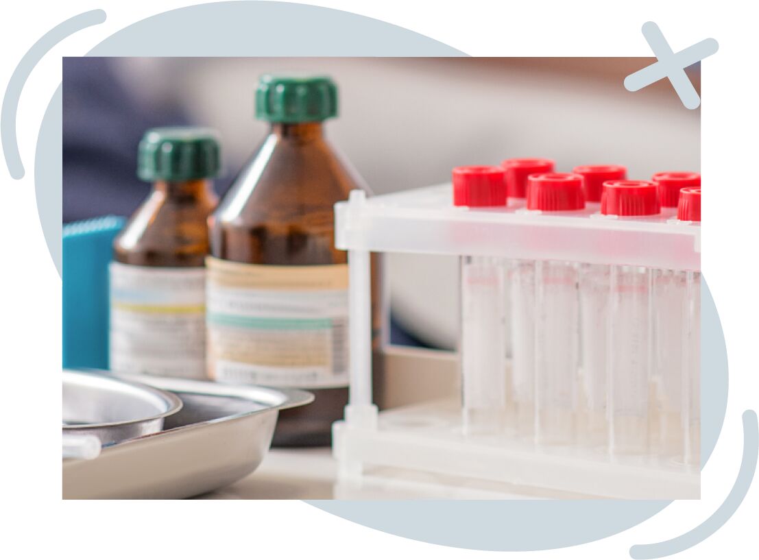 Close-up of lab equipment including a rack of clear test tubes with red caps, brown reagent bottles with green lids, and a metal tray on a countertop.