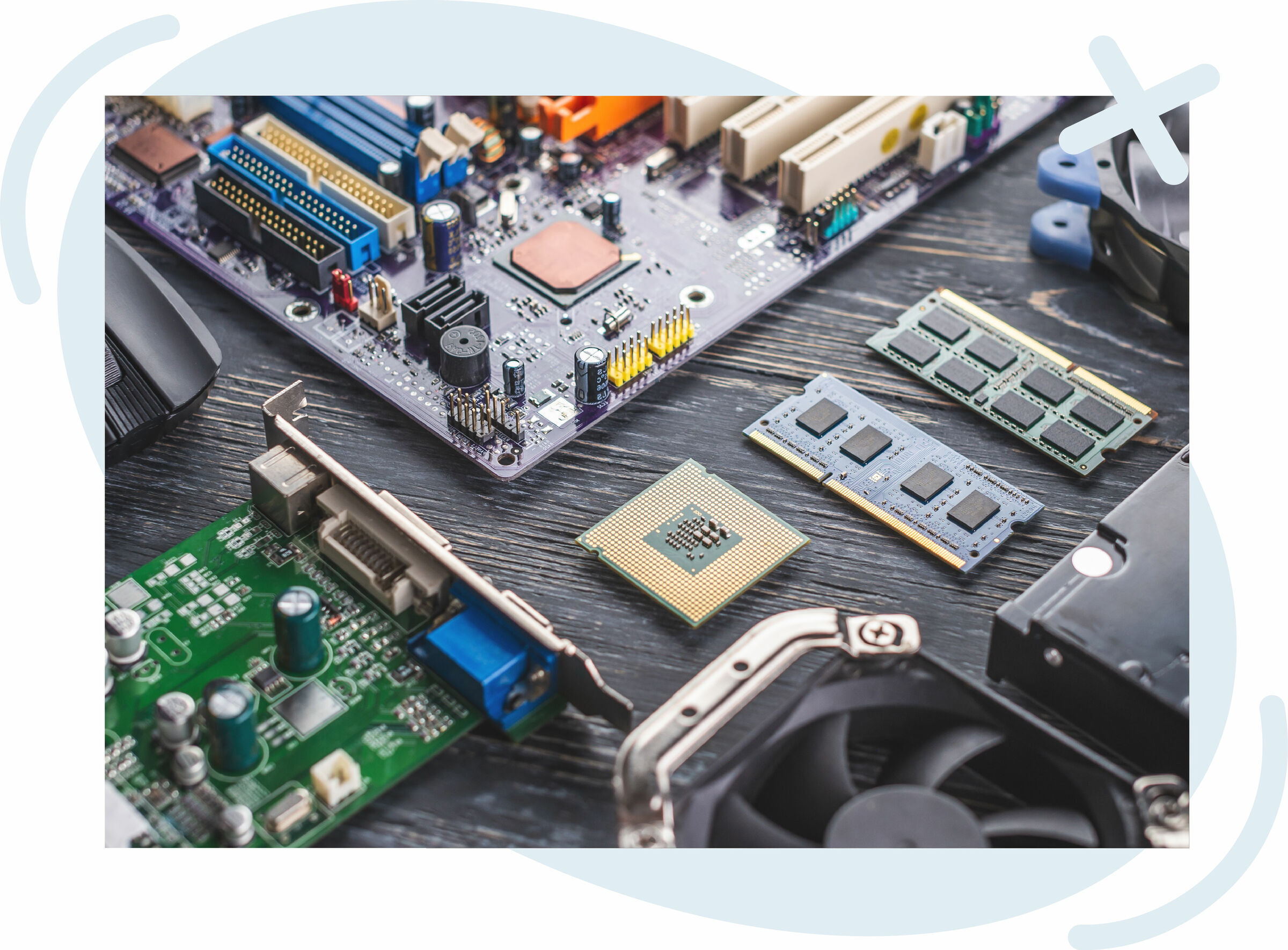 Assorted computer hardware components laid out on a dark wooden surface, including a motherboard, CPU, RAM sticks, graphics card, cooling fan, and storage drive.