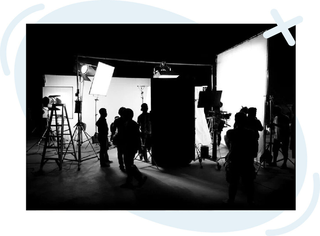 Behind-the-scenes view of a film or photo shoot set with crew silhouettes and large studio lights.