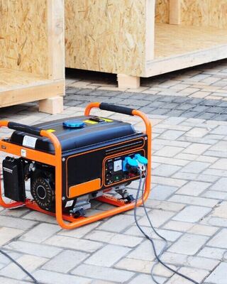 Portable orange-and-black generator with power cords on a paved surface near unfinished wooden structures.