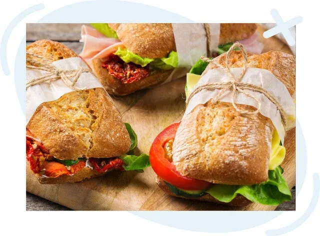 Assorted rustic sandwiches wrapped with parchment and twine on a wooden board.
