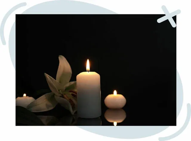Three lit white candles with a white lily on a glossy black surface against a dark background.