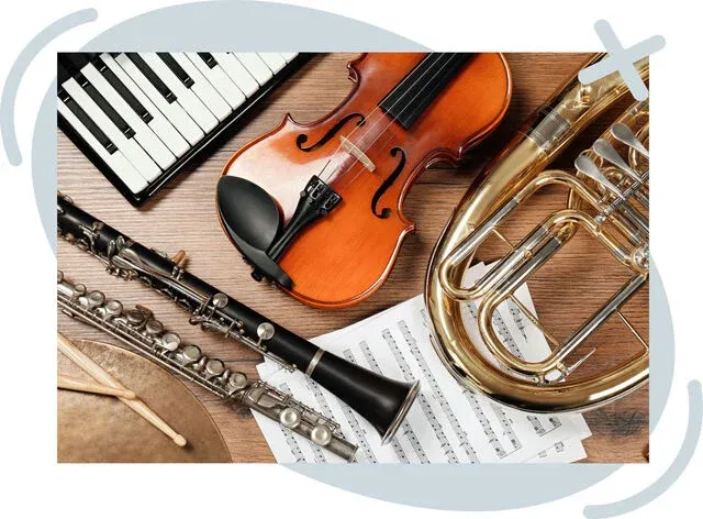 Assortment of musical instruments and sheet music on a wooden surface, including a violin, clarinet, flute, brass instrument, keyboard, and drumsticks.