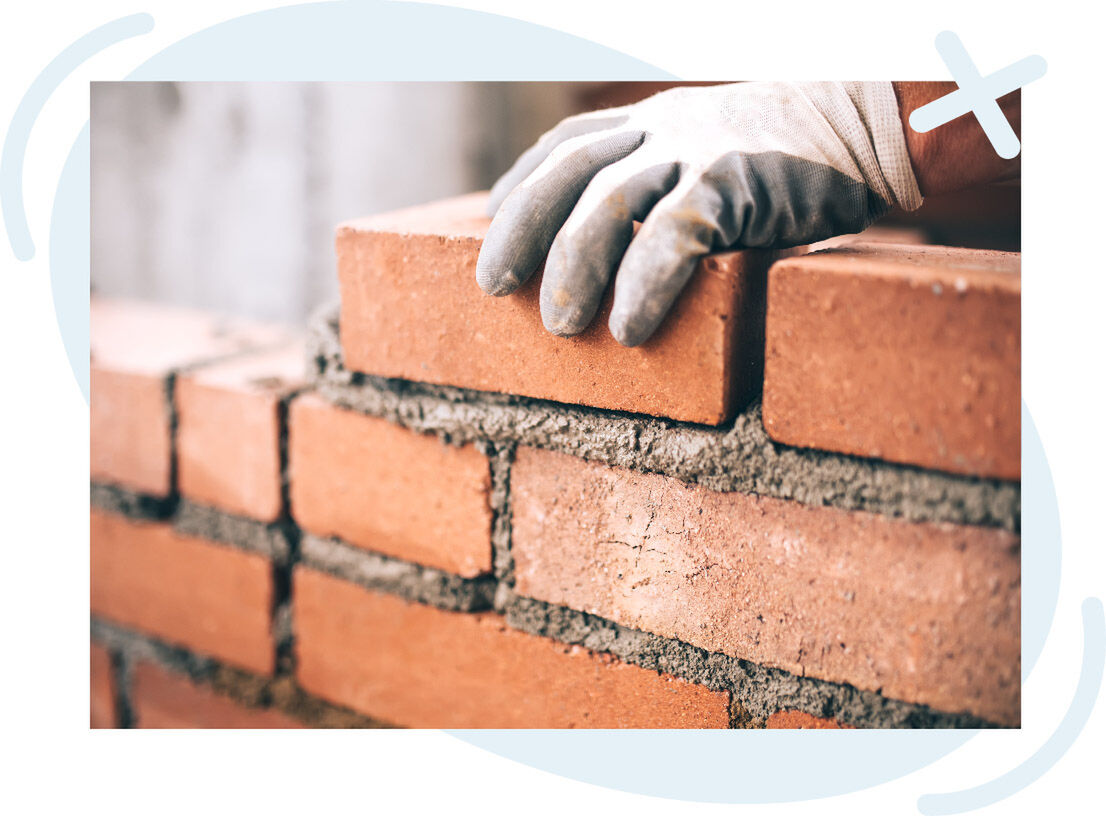 Close-up of a gloved hand placing a red brick onto a wall with fresh gray mortar.