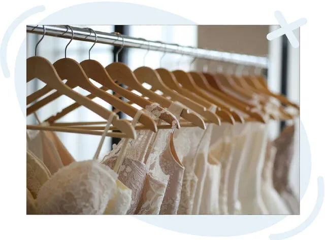 Row of white wedding dresses hanging on wooden hangers in a boutique.