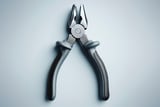 Close-up of a pair of pliers with rubberized gray handles on a light background.