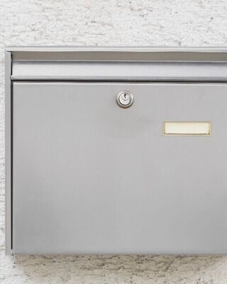 Wall-mounted stainless steel mailbox with a slot and key lock on a textured white wall.