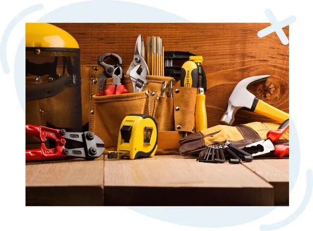 Assorted hand tools and safety gear arranged on a wooden workbench in front of a wood plank wall.