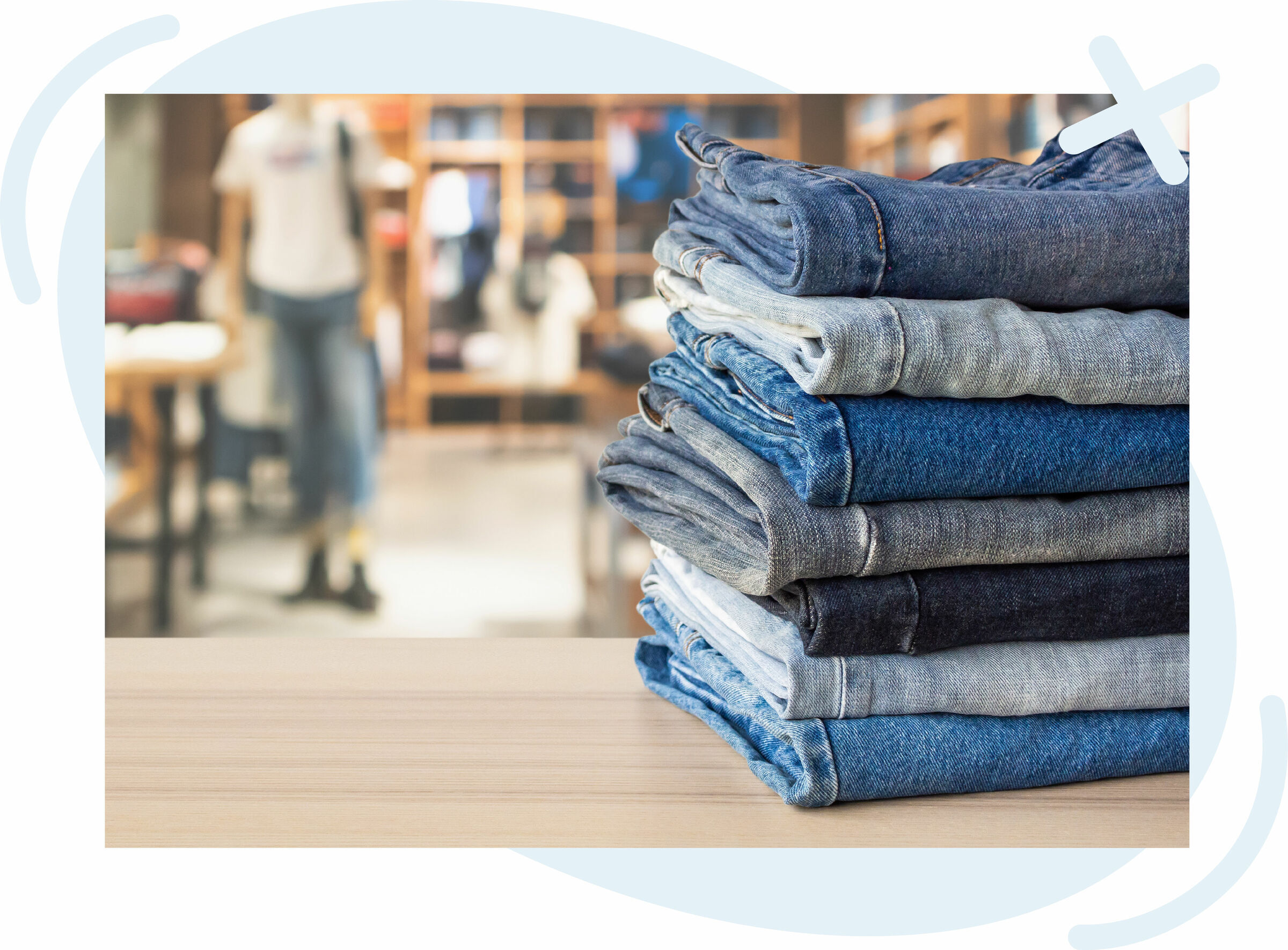 Stack of folded denim jeans on a wooden table inside a clothing store.