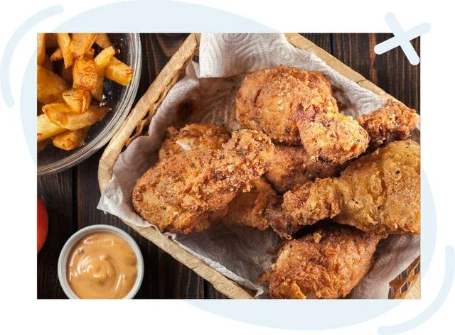 Basket of crispy fried chicken pieces with fries and dipping sauce on a wooden table.